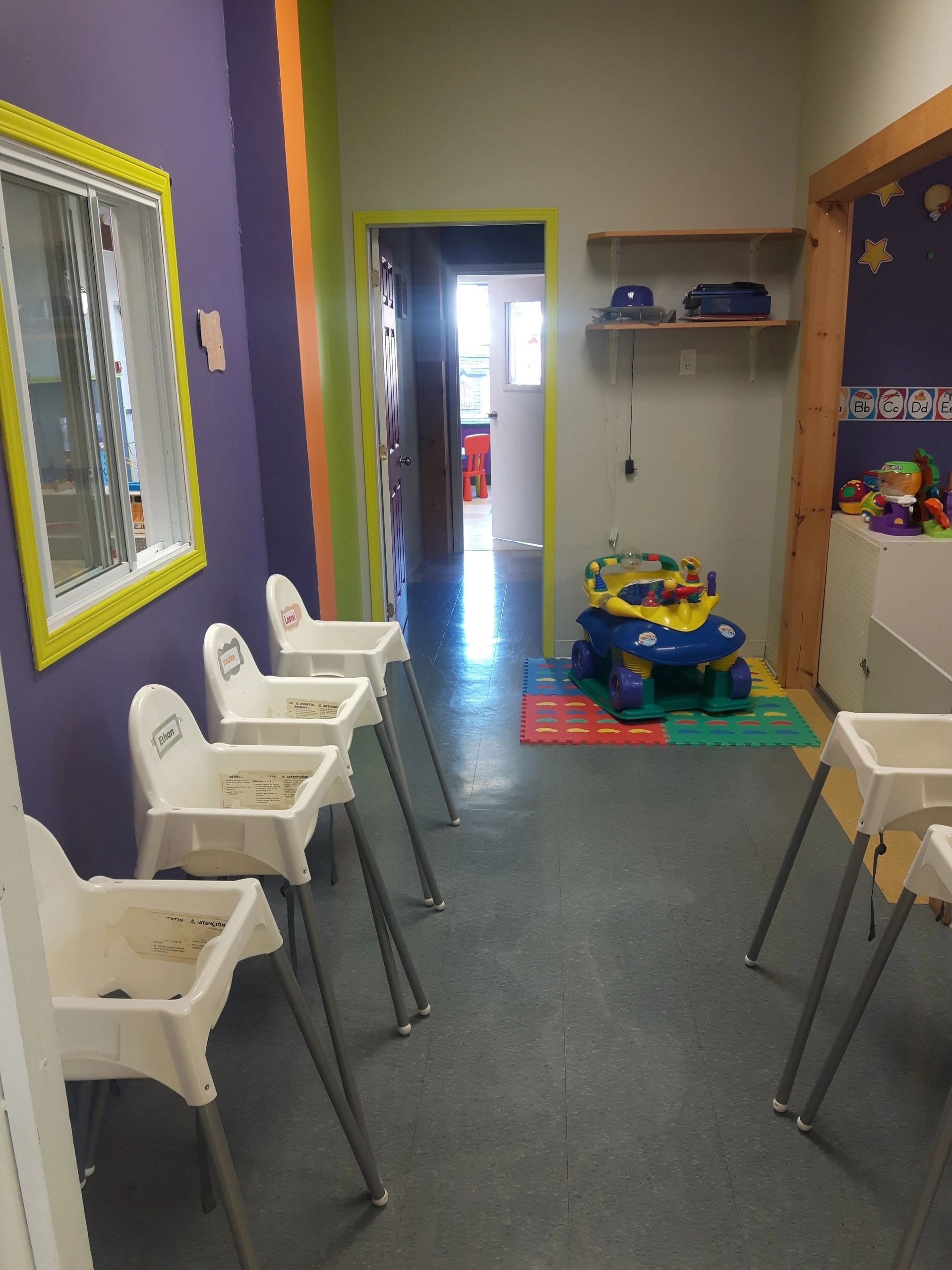 Arnprior infant room with white high chairs, colourful walls, and an activity toy on a foam mat.